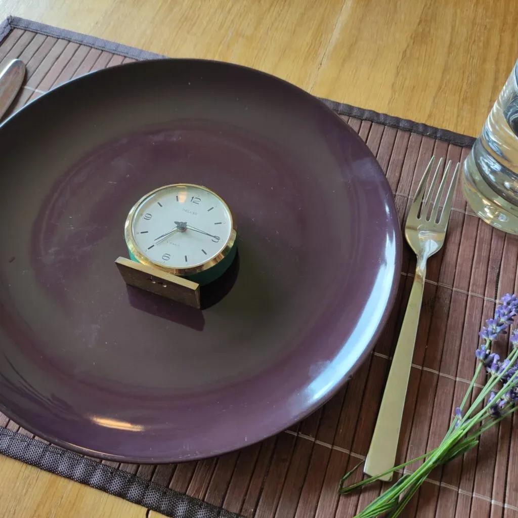 Uhr auf Teller, daneben Besteck und Lavendel. Tischdekoration kombiniert Zeit und Natur.