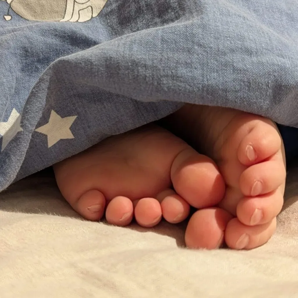 Kinderfüße unter blauer Decke mit Sternenmotiv im Bett.